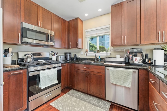 kitchen with dark stone counters, wood-type flooring, stainless steel appliances, and sink