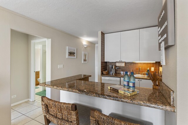 kitchen with dark stone counters, white dishwasher, tasteful backsplash, kitchen peninsula, and white cabinets