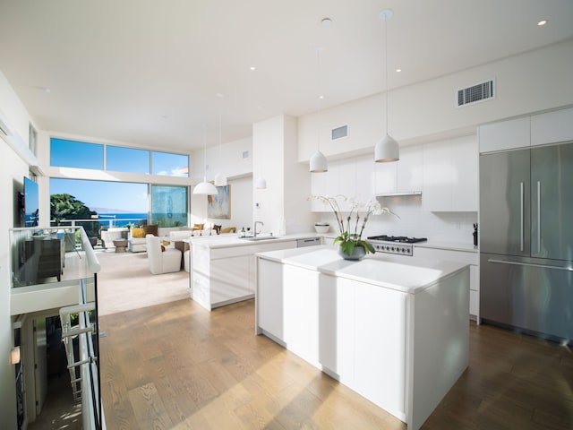 kitchen with backsplash, white cabinets, sink, hanging light fixtures, and built in refrigerator