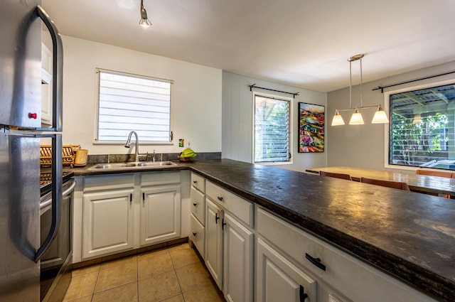 kitchen featuring sink, stainless steel fridge, white cabinetry, decorative light fixtures, and light tile patterned floors