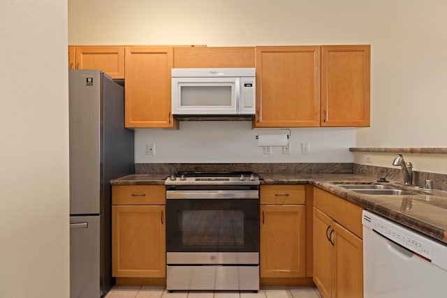 kitchen featuring sink, dark stone countertops, light tile patterned floors, and appliances with stainless steel finishes