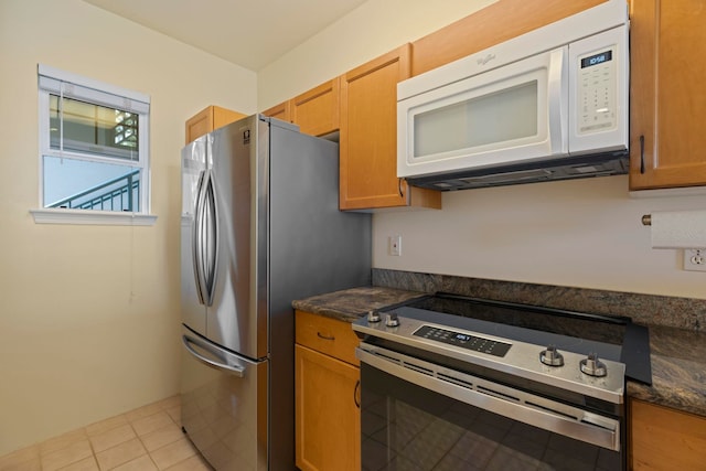 kitchen featuring light tile patterned flooring, dark stone countertops, and stainless steel appliances