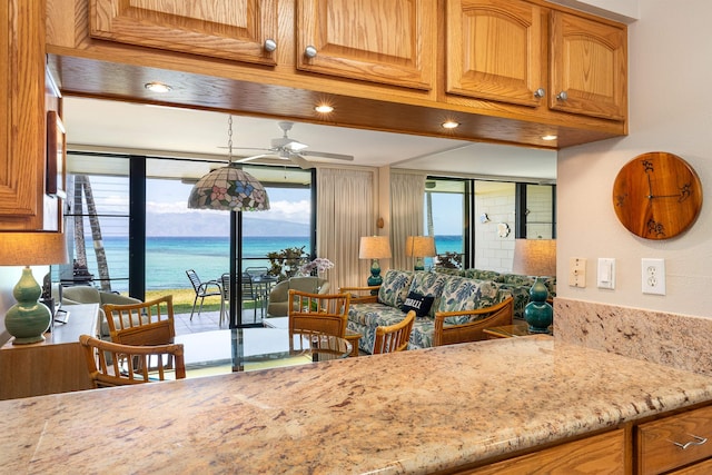 kitchen featuring ceiling fan, a water view, and light stone counters