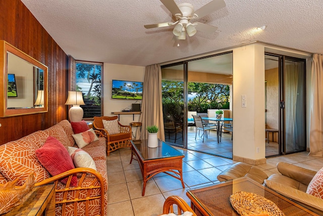 living area with a ceiling fan, light tile patterned flooring, wood walls, and a textured ceiling