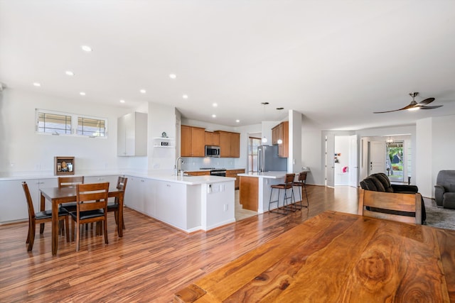 kitchen featuring a breakfast bar, appliances with stainless steel finishes, hanging light fixtures, light hardwood / wood-style floors, and kitchen peninsula