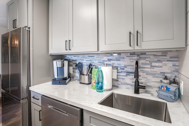 kitchen with backsplash, light stone countertops, sink, and appliances with stainless steel finishes