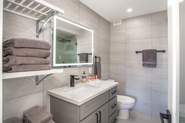 bathroom with tile patterned floors, vanity, a shower with door, tile walls, and toilet