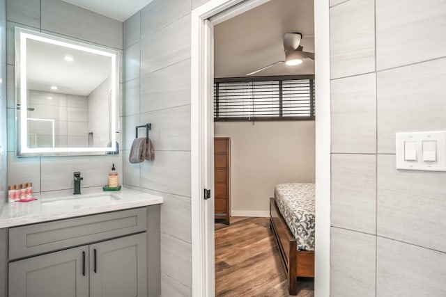 bathroom with hardwood / wood-style flooring, vanity, ceiling fan, and tile walls