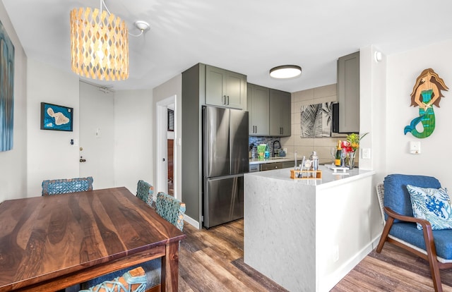 kitchen with backsplash, dark hardwood / wood-style floors, decorative light fixtures, kitchen peninsula, and stainless steel refrigerator