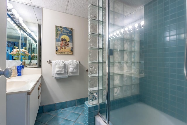 bathroom featuring vanity, baseboards, bath / shower combo with glass door, tile patterned flooring, and a paneled ceiling