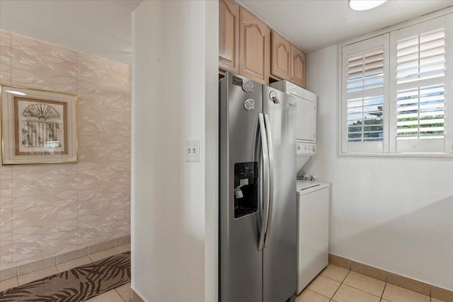 kitchen featuring light tile patterned floors, stainless steel fridge, light brown cabinets, and stacked washer and dryer