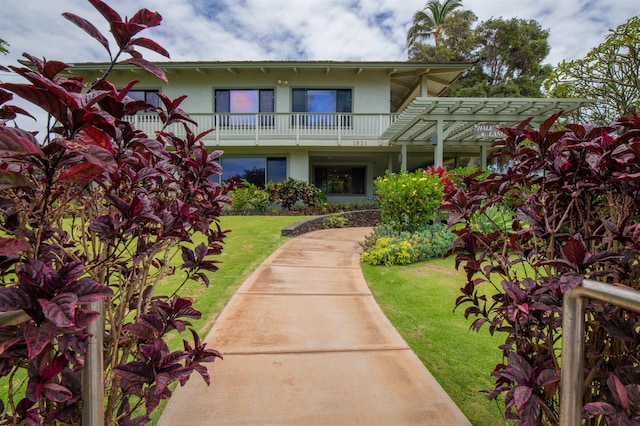 exterior space with a lawn, a pergola, stucco siding, and a balcony