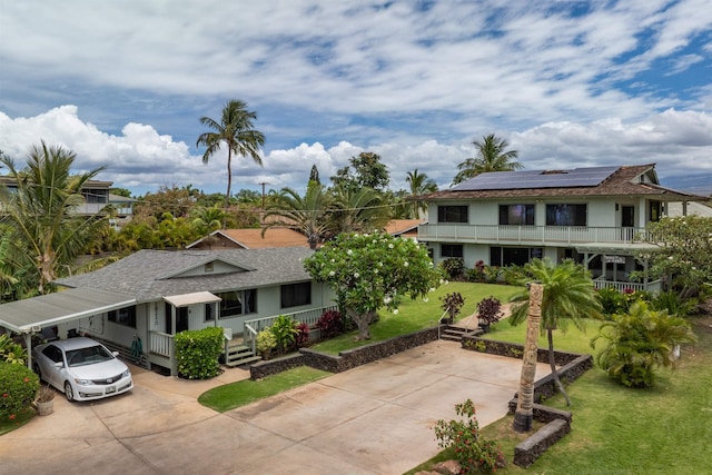 view of front facade with driveway, solar panels, roof with shingles, a front yard, and an attached carport