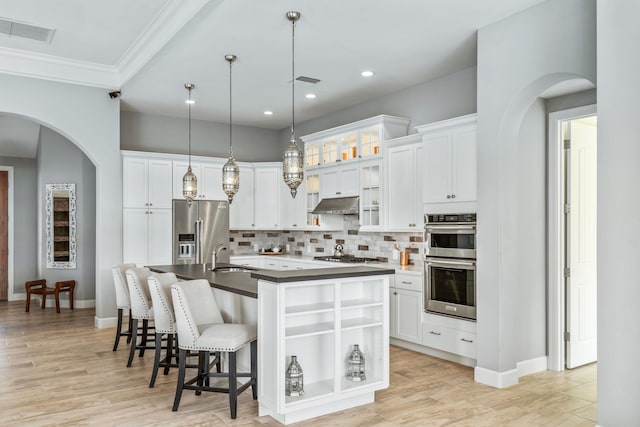 kitchen with tasteful backsplash, stainless steel appliances, a center island with sink, light hardwood / wood-style floors, and white cabinetry