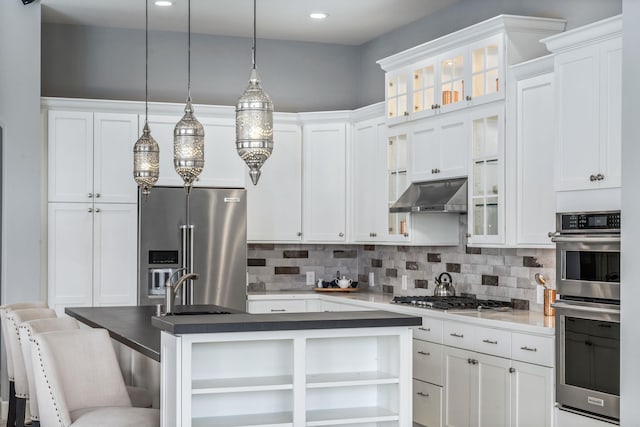 kitchen featuring white cabinetry, appliances with stainless steel finishes, decorative light fixtures, and a breakfast bar area