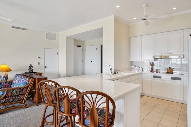 kitchen with a sink, visible vents, under cabinet range hood, tile countertops, and a peninsula