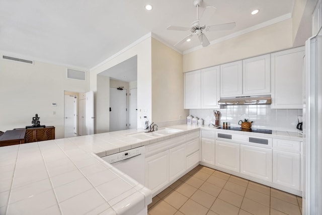 kitchen with a sink, tile counters, under cabinet range hood, and visible vents