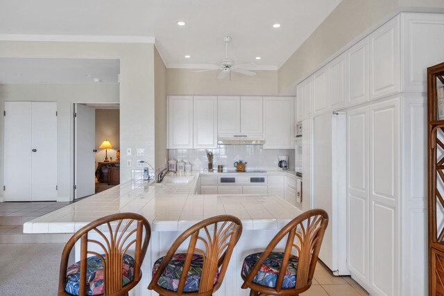 kitchen with under cabinet range hood, ceiling fan, white cabinetry, tile countertops, and white appliances
