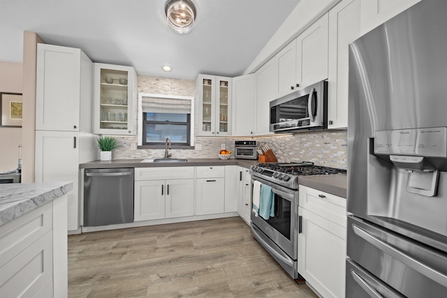 kitchen with light wood-style flooring, a sink, white cabinetry, stainless steel appliances, and decorative backsplash