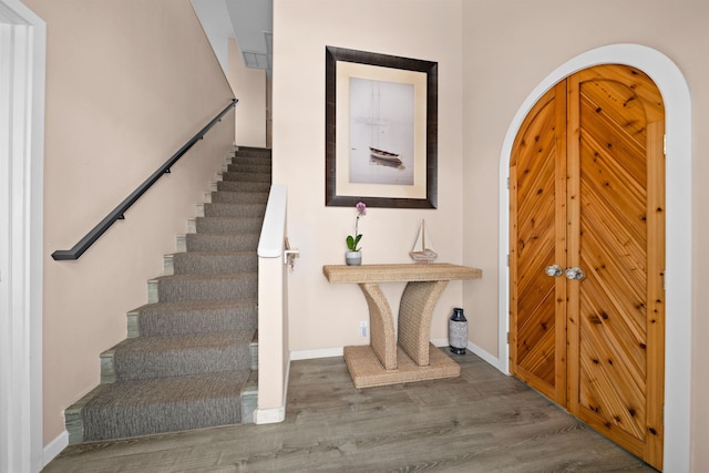 foyer entrance featuring baseboards, arched walkways, wood finished floors, and stairs