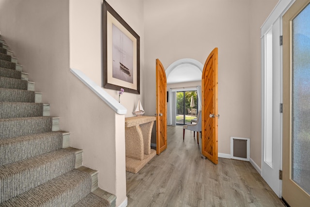 interior space with arched walkways, light wood-style flooring, stairs, and baseboards