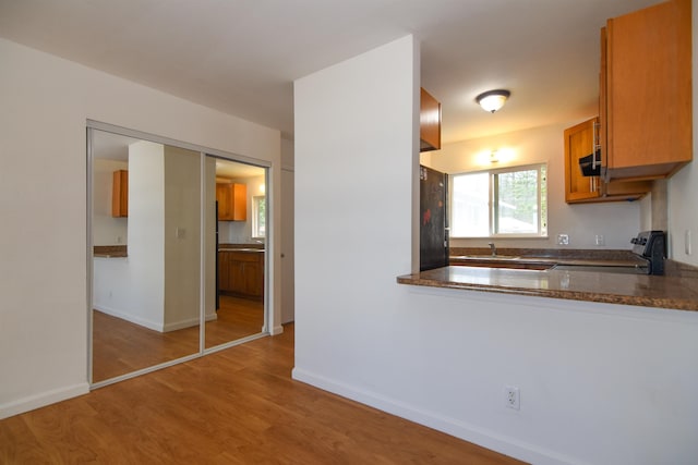 kitchen featuring kitchen peninsula, black refrigerator, sink, stove, and light hardwood / wood-style floors