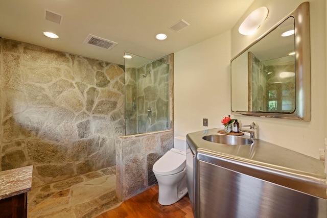 bathroom featuring a tile shower, vanity, toilet, and wood-type flooring