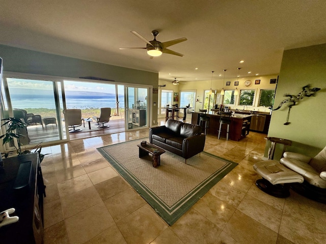 tiled living room featuring ceiling fan, a healthy amount of sunlight, and a water view