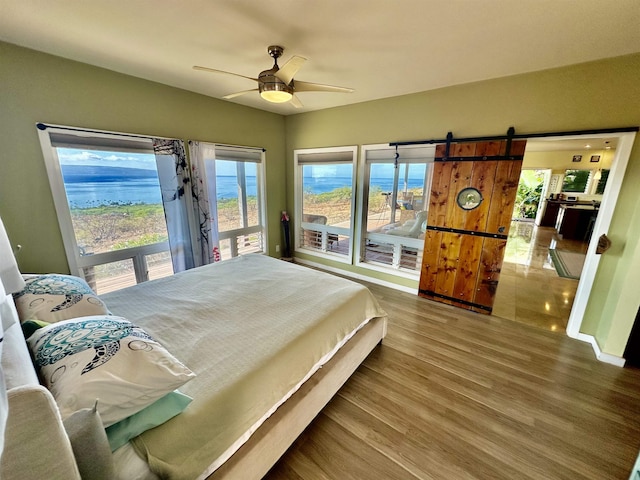 bedroom with ceiling fan, wood-type flooring, a barn door, and multiple windows