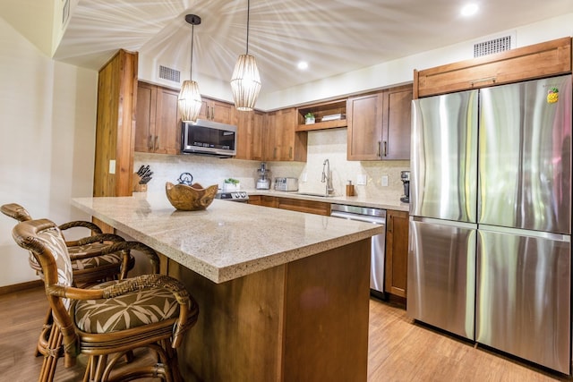 kitchen with pendant lighting, a breakfast bar, appliances with stainless steel finishes, tasteful backsplash, and light stone counters