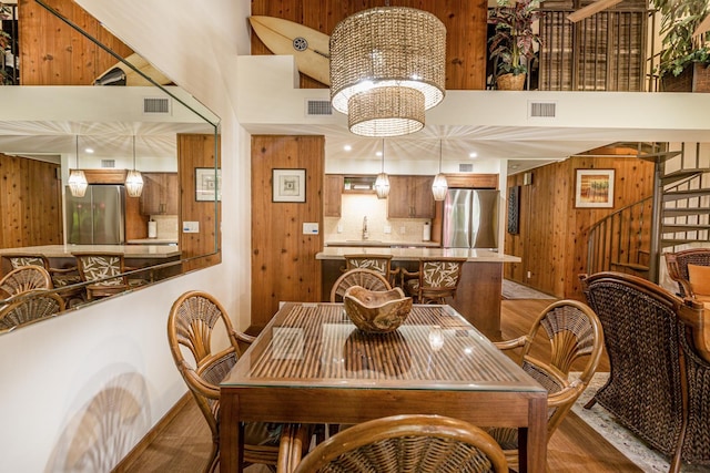 dining space with wood walls, a towering ceiling, a chandelier, and wood-type flooring