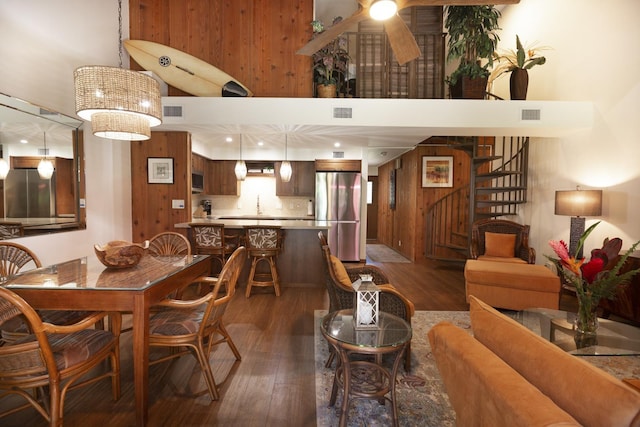 dining room with ceiling fan, dark hardwood / wood-style flooring, a towering ceiling, and wooden walls