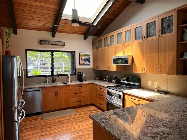 kitchen with stone countertops, stainless steel appliances, vaulted ceiling with skylight, light hardwood / wood-style flooring, and sink