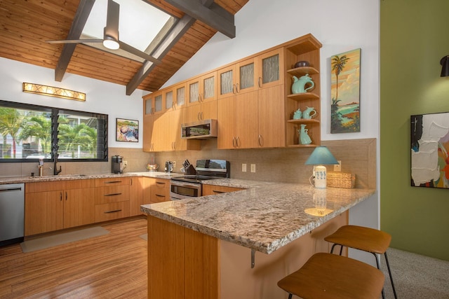 kitchen with light stone counters, lofted ceiling with skylight, stainless steel appliances, and kitchen peninsula