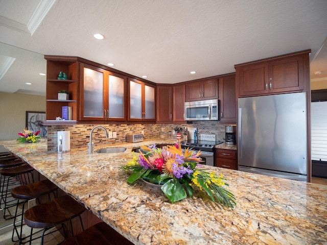 kitchen with decorative backsplash, light stone countertops, ornamental molding, stainless steel appliances, and sink