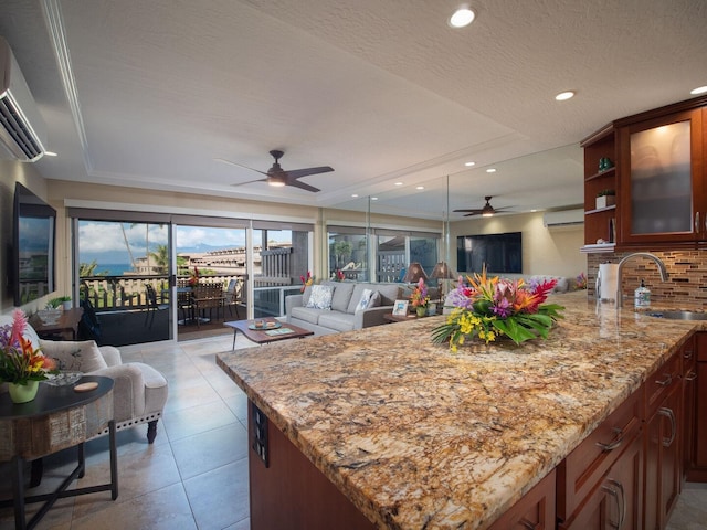 kitchen with kitchen peninsula, a raised ceiling, light stone counters, and sink