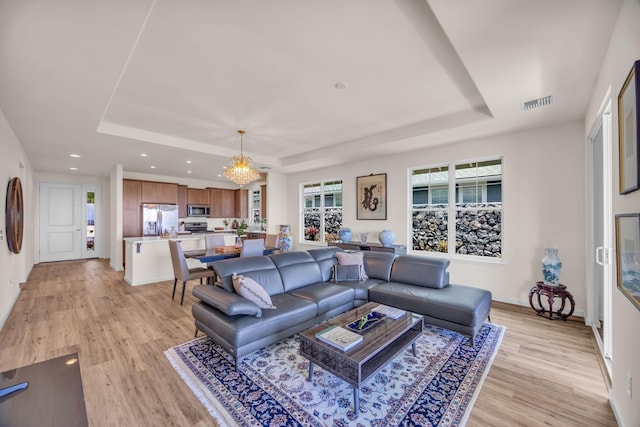 living area featuring a tray ceiling, light wood-type flooring, recessed lighting, a chandelier, and baseboards