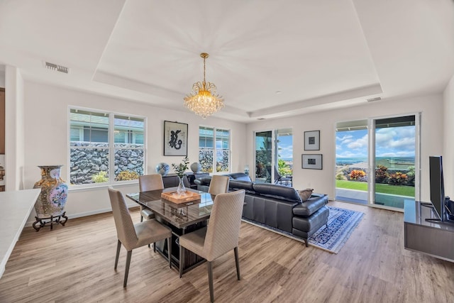 dining room featuring a raised ceiling, a chandelier, and light wood-type flooring
