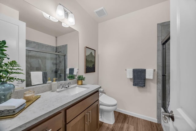 bathroom with tiled shower, wood finished floors, toilet, and vanity
