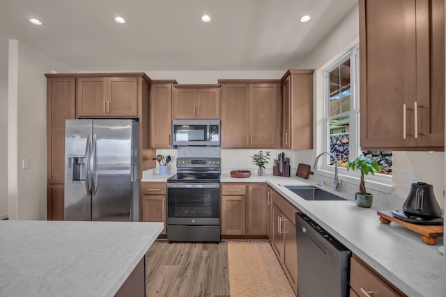 kitchen featuring stainless steel appliances, a sink, light countertops, recessed lighting, and light wood finished floors