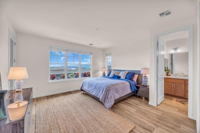 bedroom with light wood finished floors, baseboards, and connected bathroom