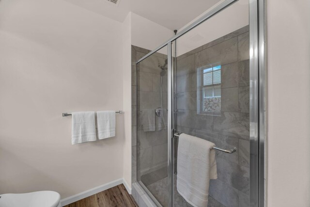 full bath featuring toilet, baseboards, wood finished floors, and a shower stall