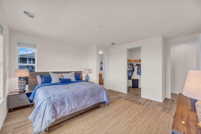 bedroom featuring light wood-style floors, baseboards, a walk in closet, and a closet