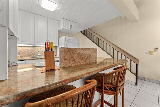 kitchen featuring tasteful backsplash, light tile patterned flooring, sink, white cabinetry, and light stone counters