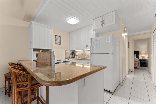 kitchen with kitchen peninsula, white cabinets, a kitchen breakfast bar, light stone countertops, and white fridge