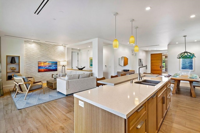 kitchen featuring pendant lighting, sink, a center island with sink, and light hardwood / wood-style flooring