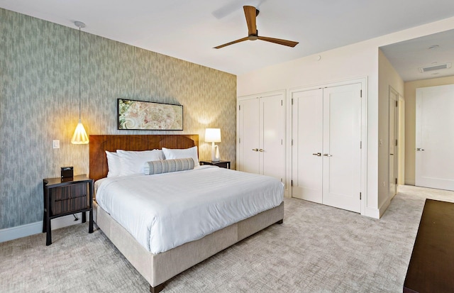 bedroom with multiple closets, light colored carpet, and ceiling fan