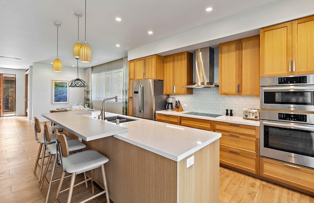 kitchen with appliances with stainless steel finishes, sink, an island with sink, and wall chimney range hood