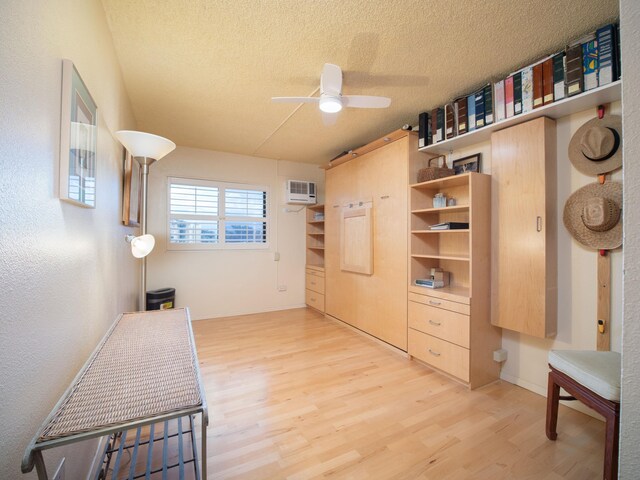 interior space featuring a textured ceiling, an AC wall unit, ceiling fan, and light hardwood / wood-style floors