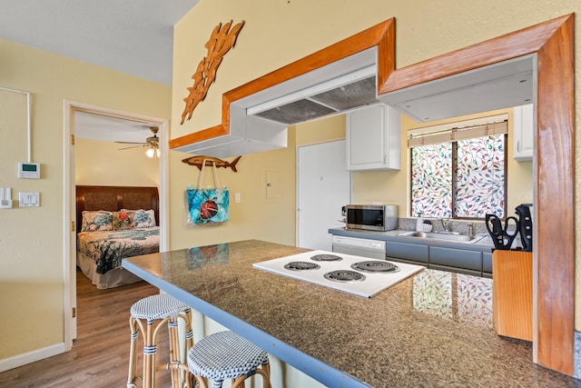 kitchen with ceiling fan, white cabinetry, sink, light wood-type flooring, and a breakfast bar